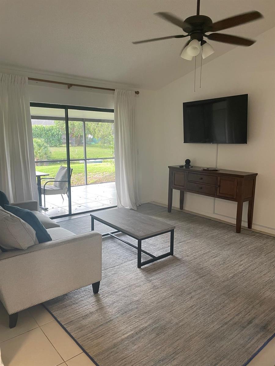 A living room features a sofa, coffee table, wall-mounted television, and sliding doors to a patio — 12726 Spinnaker Lane, Wellington FL 33414, WELLINGTON, FL