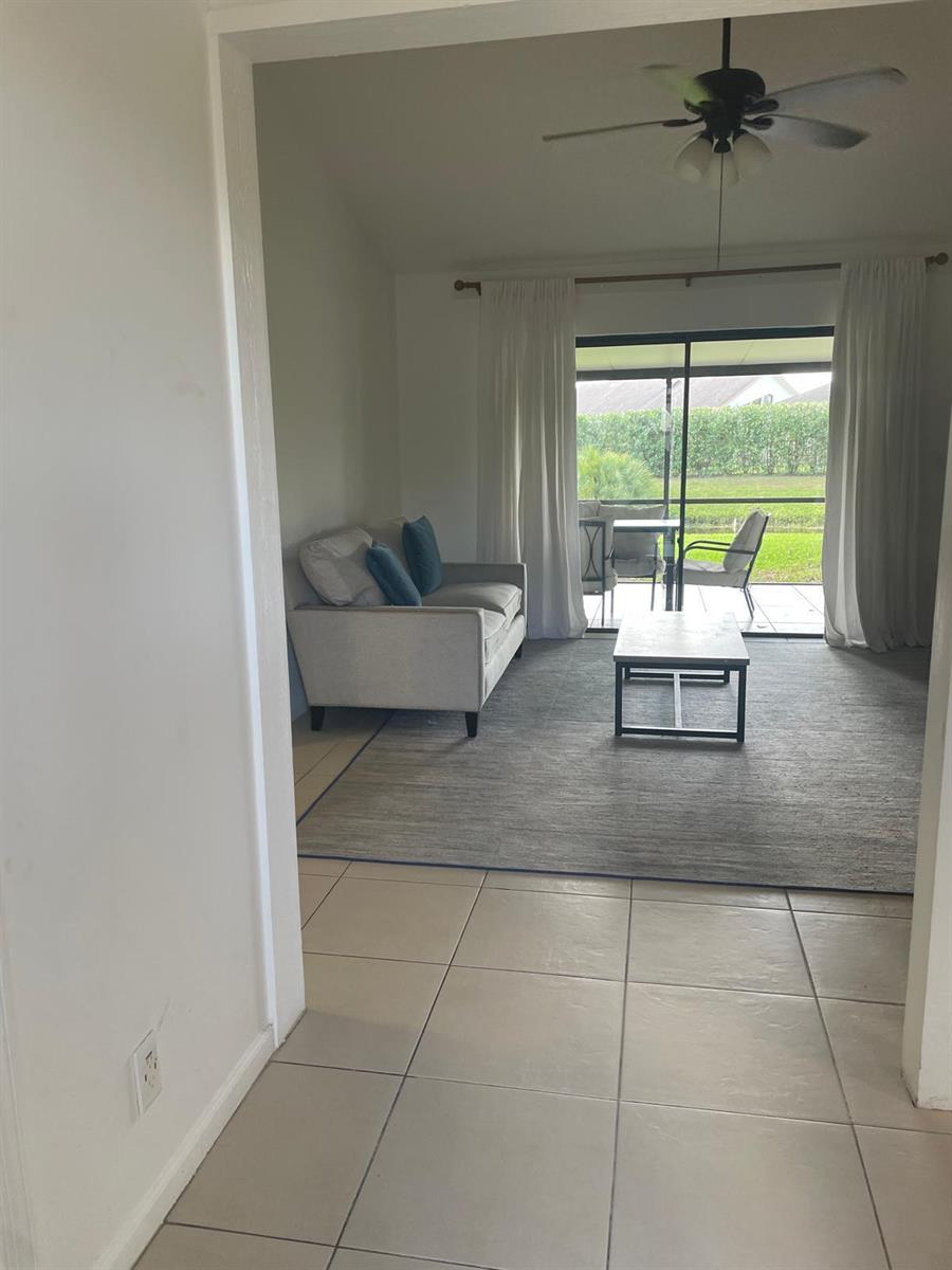A living room with tile floors, a gray area rug, a sofa, and a sliding door — 12726 Spinnaker Lane, Wellington FL 33414, WELLINGTON, FL