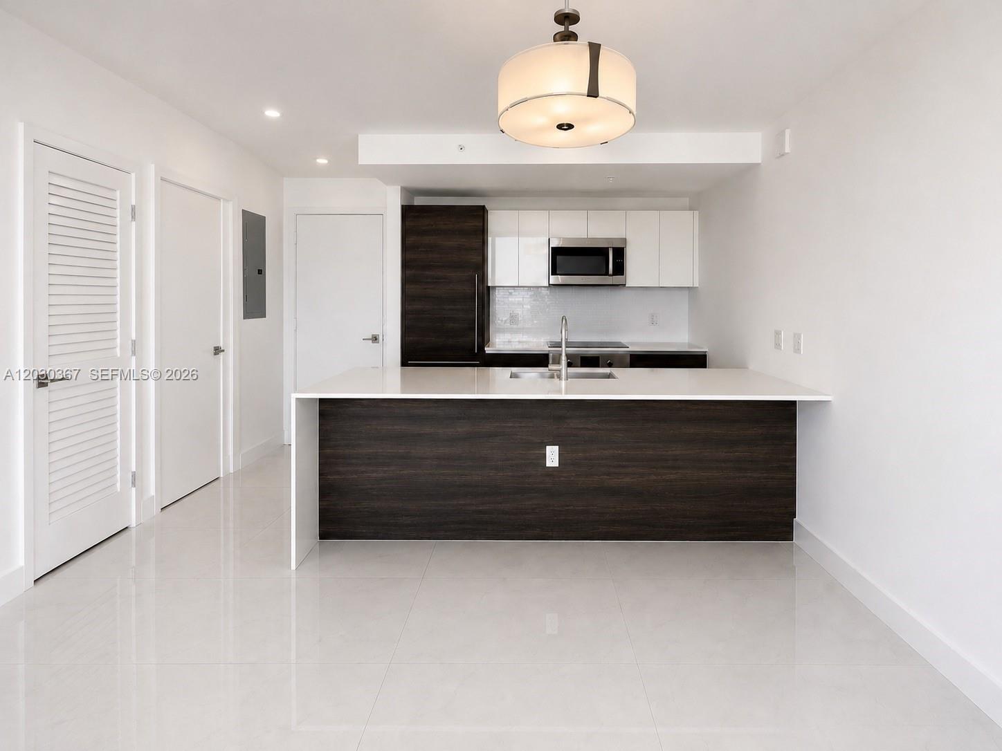 A modern kitchen features a dark wood island, white cabinetry, and light-colored tile flooring — 301 Altara Ave # 529, Coral Gables FL 33146, CORAL GABLES, FL