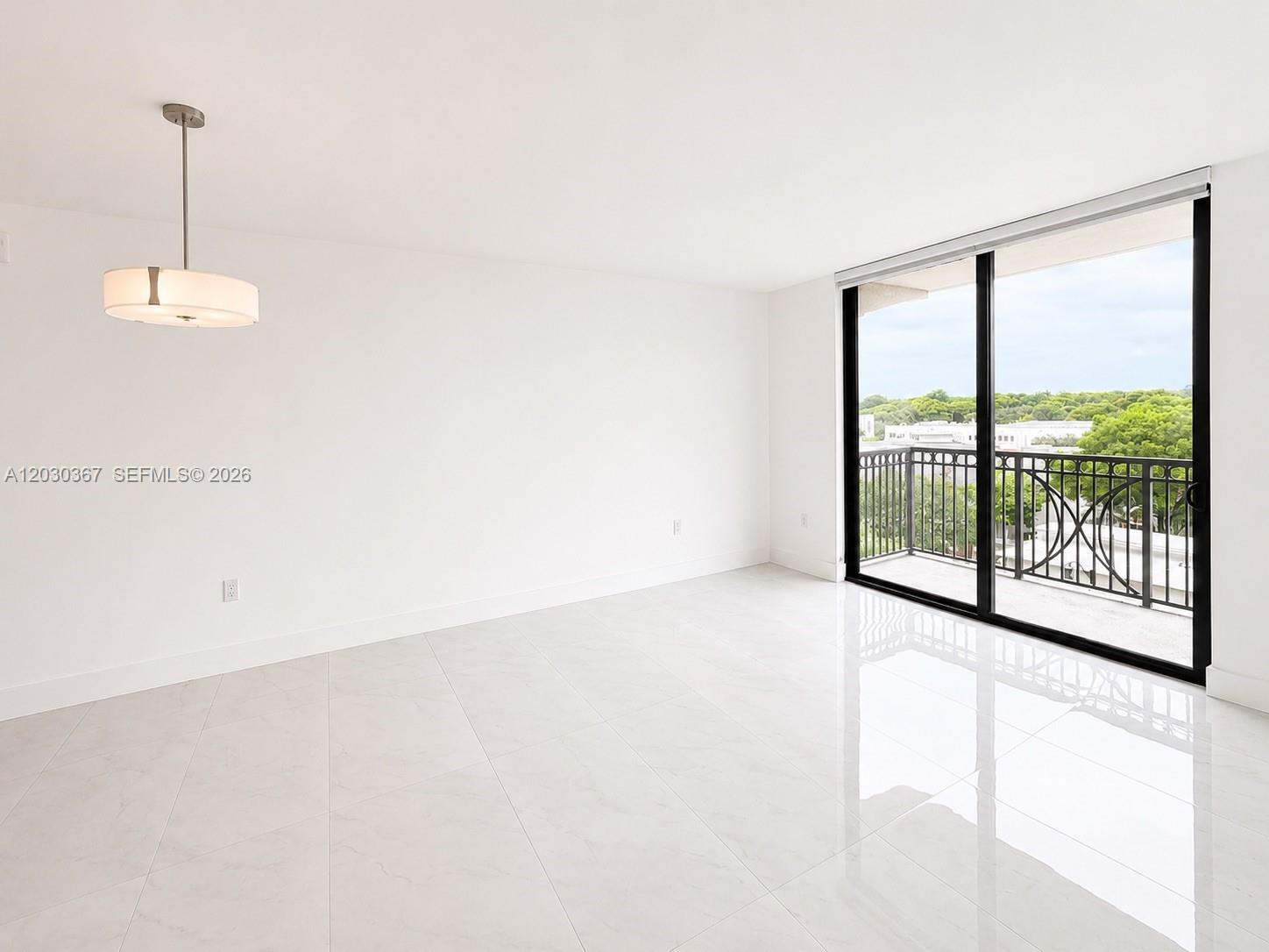 An empty room features white tile flooring, a modern pendant light, and a sliding glass door — 301 Altara Ave # 529, Coral Gables FL 33146, CORAL GABLES, FL
