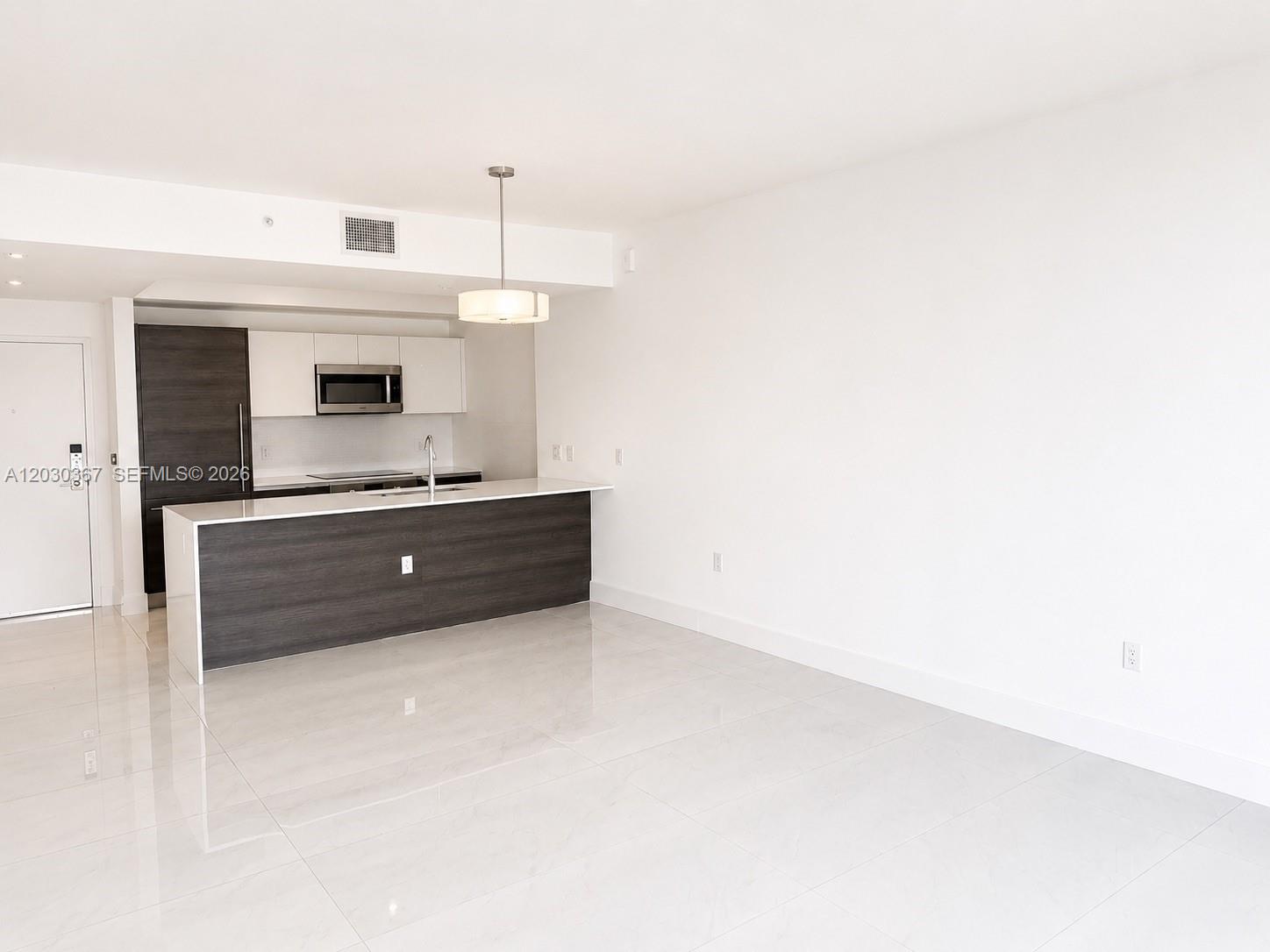 A modern kitchen with dark wood cabinetry and white countertops opens into a living area — 301 Altara Ave # 529, Coral Gables FL 33146, CORAL GABLES, FL