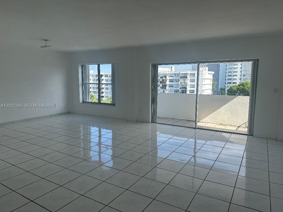 An empty room features white walls, glossy tiled floors, and a sliding glass door to a balcony — 1075 92nd St # 603, Bay Harbor Islands FL 33154, BAY HARBOR ISLANDS, FL