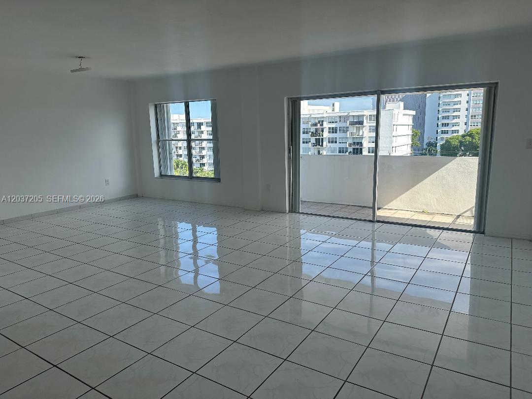 An empty room features white tiled floors, large windows, and a sliding door to a balcony — 1075 92nd St # 603, Bay Harbor Islands FL 33154, BAY HARBOR ISLANDS, FL