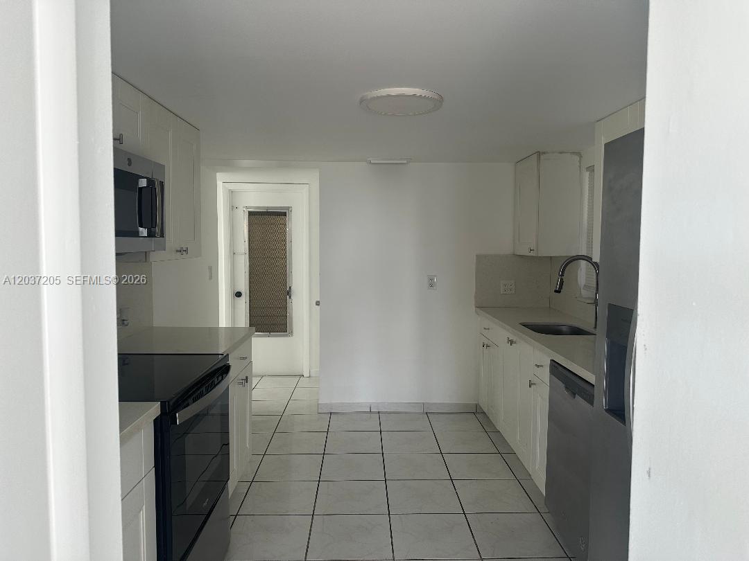A galley kitchen features white cabinets, stainless steel appliances, and light-colored floor tiles — 1075 92nd St # 603, Bay Harbor Islands FL 33154, BAY HARBOR ISLANDS, FL