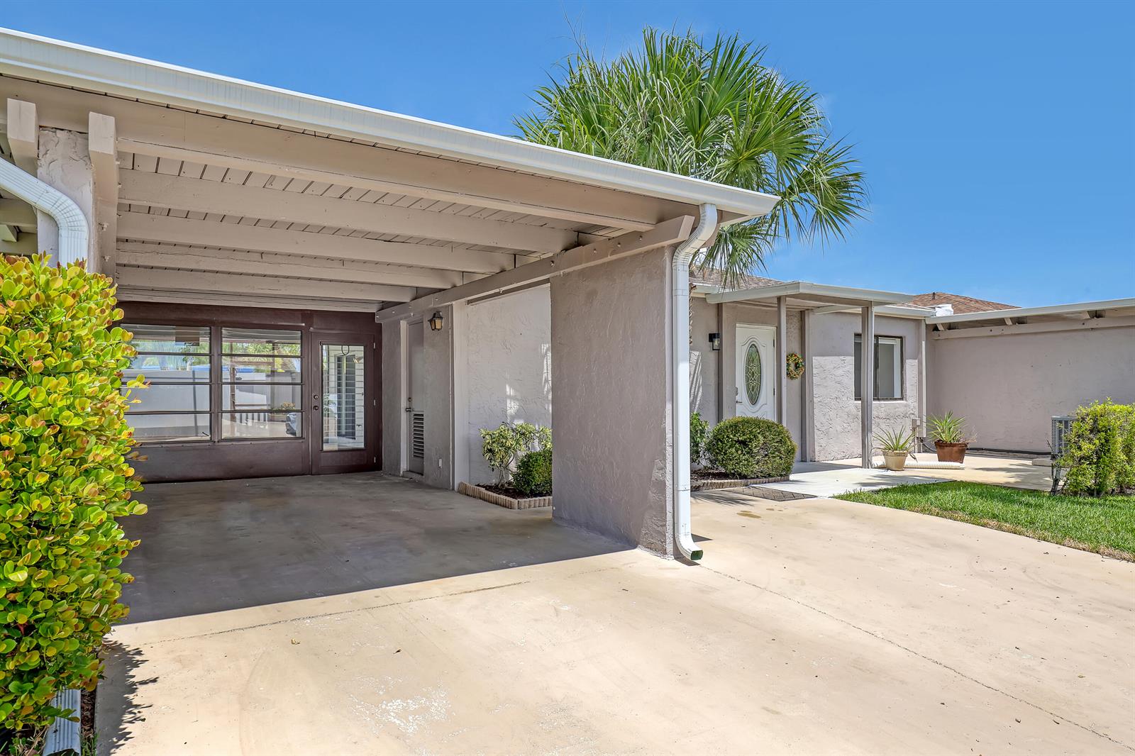 A beige house exterior features a covered carport, a concrete driveway, and a front entrance — 14735 Wildflower Lane, Delray Beach FL 33446, DELRAY BEACH, FL