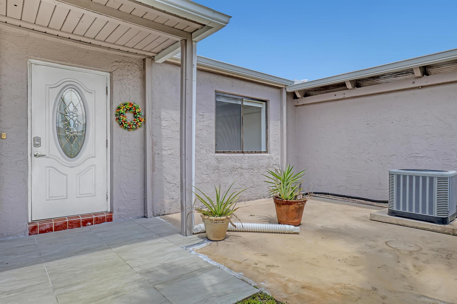 A white front door with a decorative glass insert opens onto a tiled patio area — 14735 Wildflower Lane, Delray Beach FL 33446, DELRAY BEACH, FL