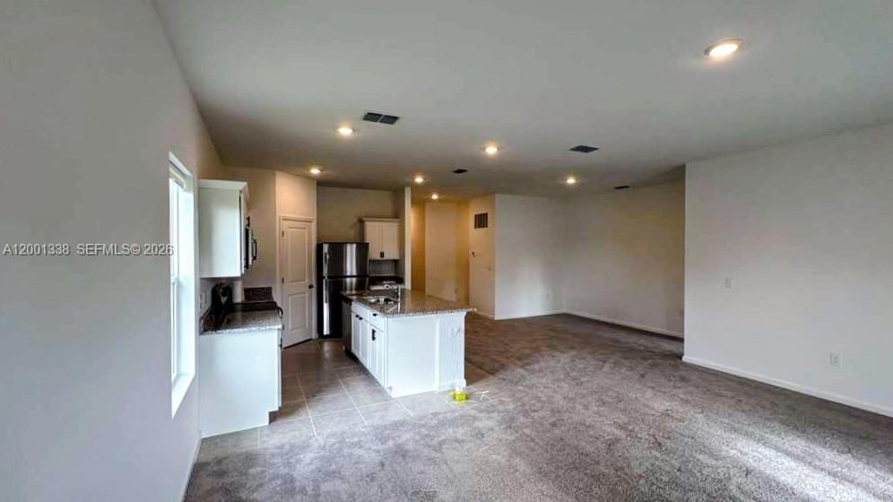 An open-concept kitchen with white cabinets and granite countertops flows into a carpeted living area — KISSIMMEE, FL