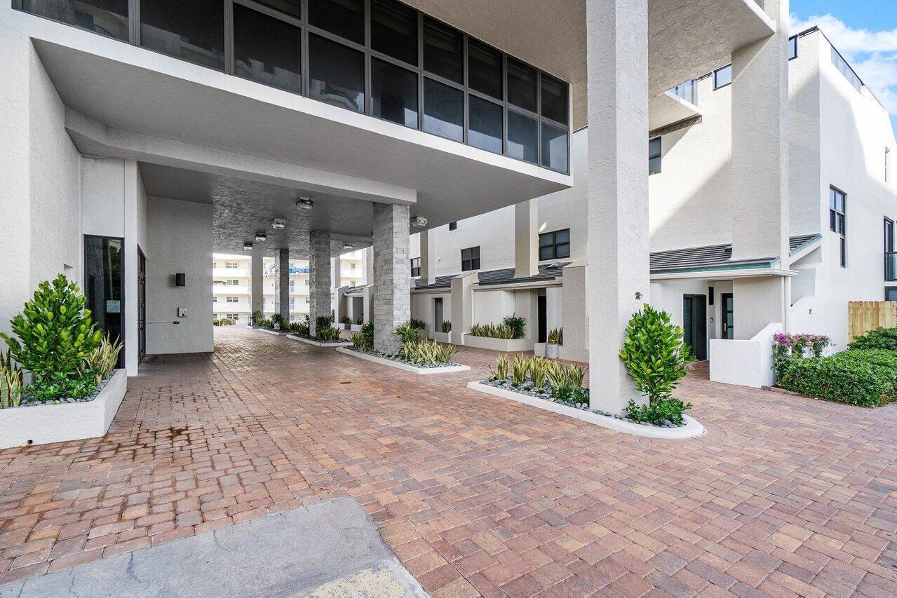 A paved driveway leads under a modern building with white stucco walls and large windows — 3115 S Ocean Boulevard # 1001, Highland Beach FL 33487, HIGHLAND BEACH, FL