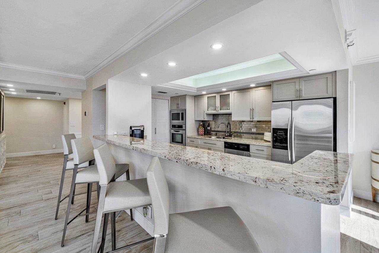 A kitchen features a granite breakfast bar, stainless steel appliances, and light-colored cabinetry — 3115 S Ocean Boulevard # 1001, Highland Beach FL 33487, HIGHLAND BEACH, FL