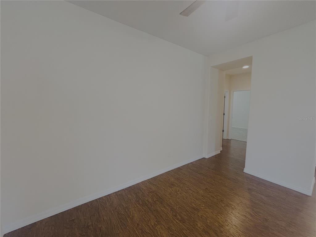 An empty room features white walls, wood-look flooring, and a doorway leading to another room — 4859 NW 35TH LANE ROAD, OCALA, FL