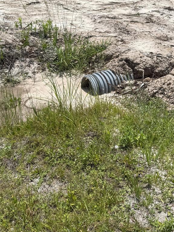 A corrugated plastic drainage pipe is partially buried in a sandy, grassy outdoor area — 1573 LAUREL AVENUE, BUNNELL, FL