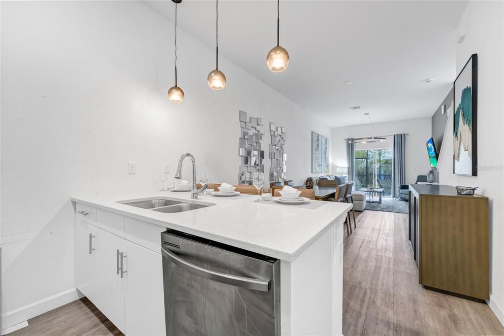 A modern kitchen island with a stainless steel dishwasher overlooks an open-concept living and dining area — 344 FAMAGUSTA DR DRIVE, DAVENPORT, FL