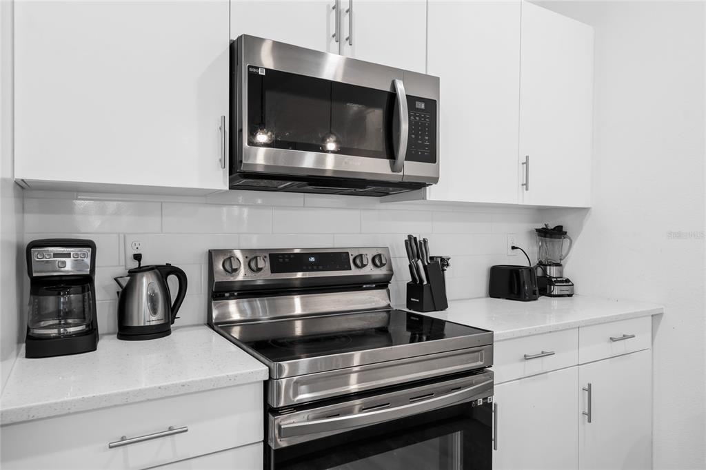 A modern kitchen features white cabinets, a stainless steel microwave, and a glass-top electric range — 344 FAMAGUSTA DR DRIVE, DAVENPORT, FL