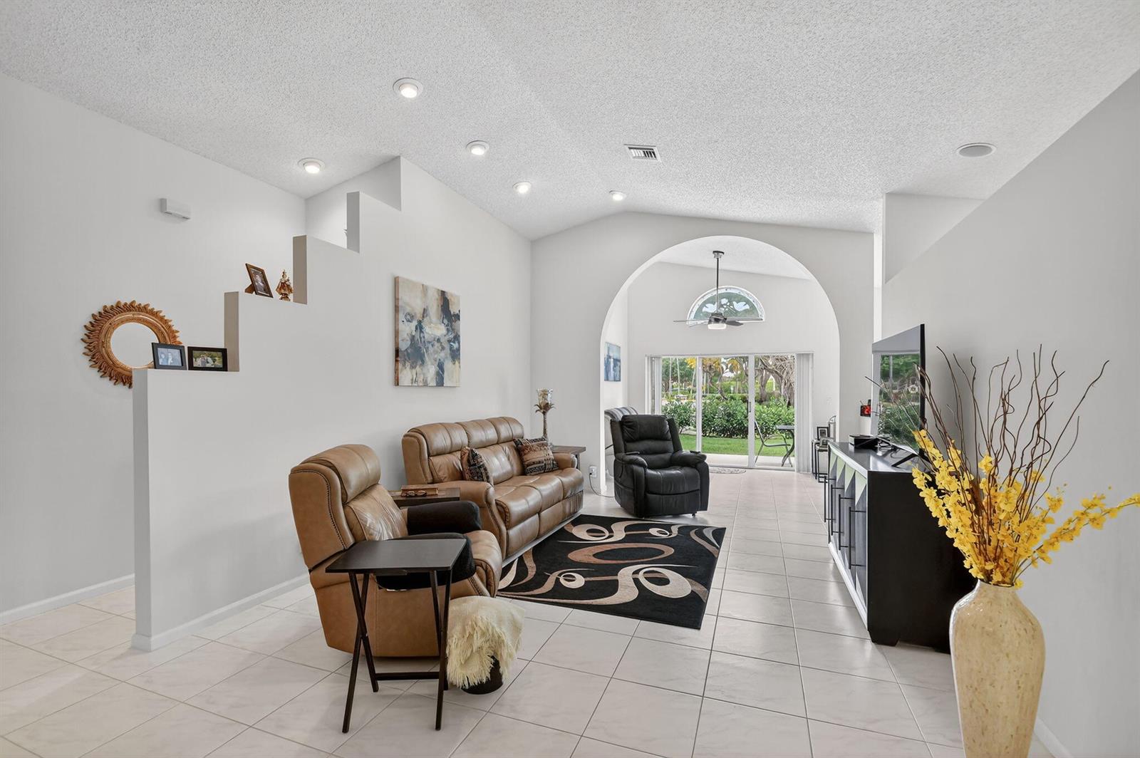A living room features a vaulted ceiling, tiled floors, leather furniture, and a large arched doorway — 9718 Harbour Lake Circle, Boynton Beach FL 33437, BOYNTON BEACH, FL