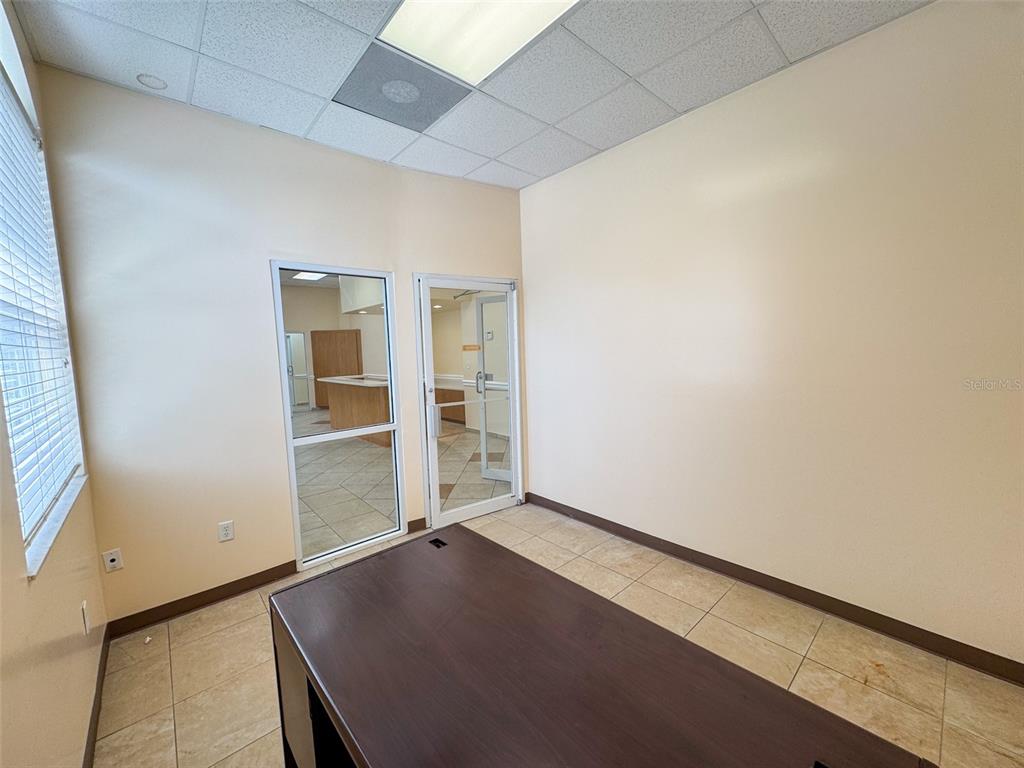 An office space features a dark desk, tile flooring, beige walls, and glass-paneled doors — 690 LAKE FOREST BOULEVARD UNIT Suite 1, SANFORD, FL