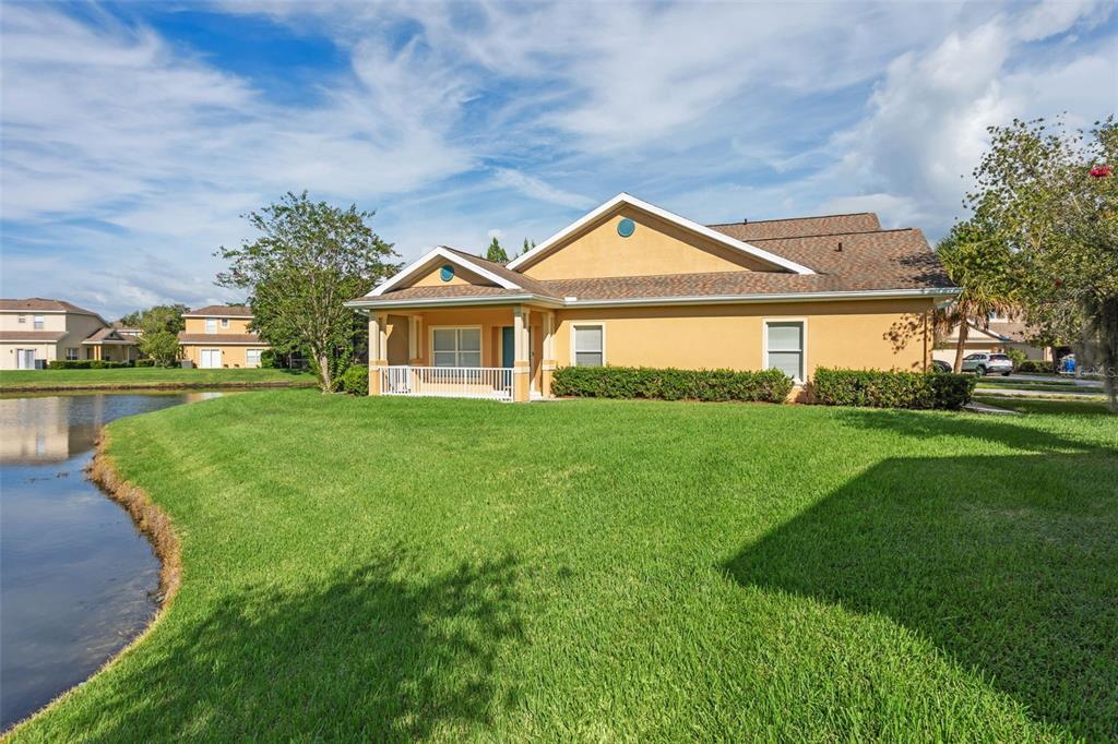 A tan house with a covered porch sits beside a pond on a grassy lot — 20312 NOBLE OAK PLACE, TAMPA, FL