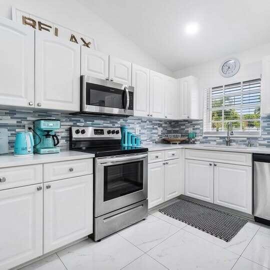 A kitchen with white cabinets, stainless steel appliances, and a blue-tiled backsplash — 1906 N N A St Street, FL 33460, FL