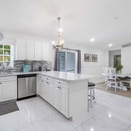 A bright kitchen features white cabinets, a central island, stainless steel appliances, and marble-look flooring — 1906 N N A St Street, FL 33460, FL