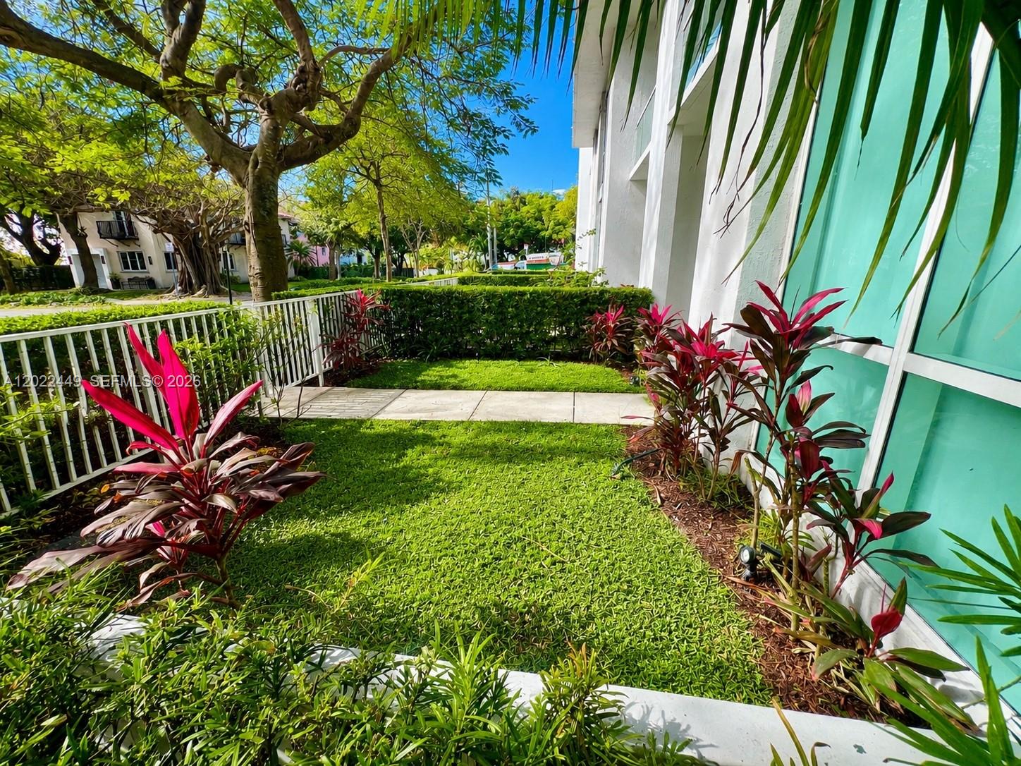 A small grassy yard with red-leafed plants sits beside a white building and fence — 1871 NW S River Dr # A04, Miami FL 33125, MIAMI, FL