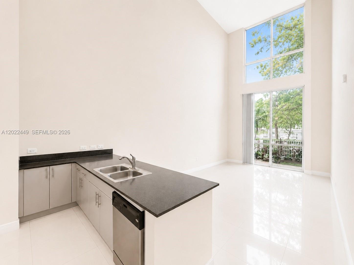 A kitchen with gray cabinets and dark countertops opens into a living area with high ceilings — 1871 NW S River Dr # A04, Miami FL 33125, MIAMI, FL