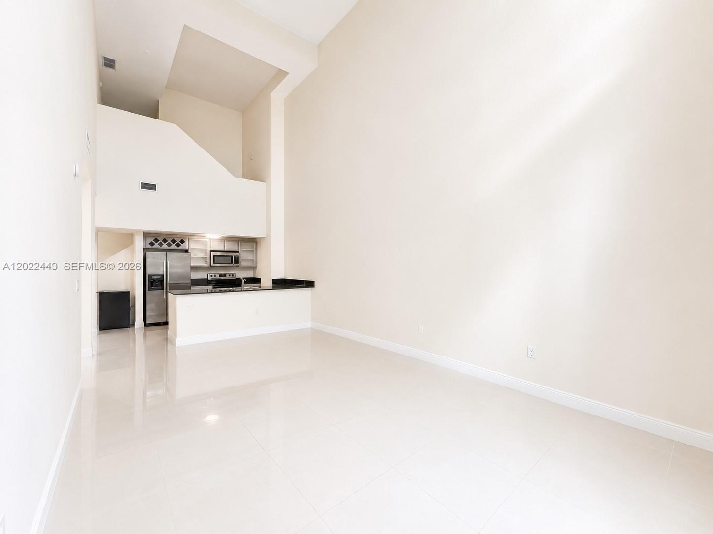 An open-concept living area features a kitchen with dark countertops and high vaulted ceilings — 1871 NW S River Dr # A04, Miami FL 33125, MIAMI, FL