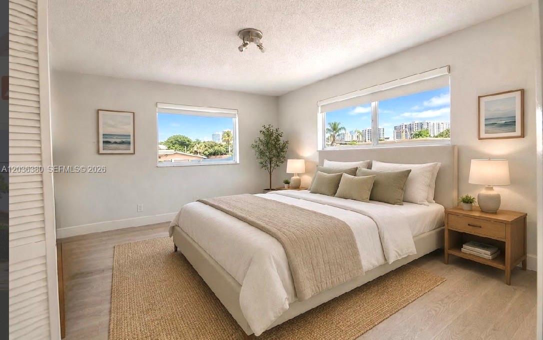 A bright bedroom features a queen bed, light wood flooring, and windows overlooking city buildings — 444 SW 4th St # 204, Miami FL 33130, MIAMI, FL