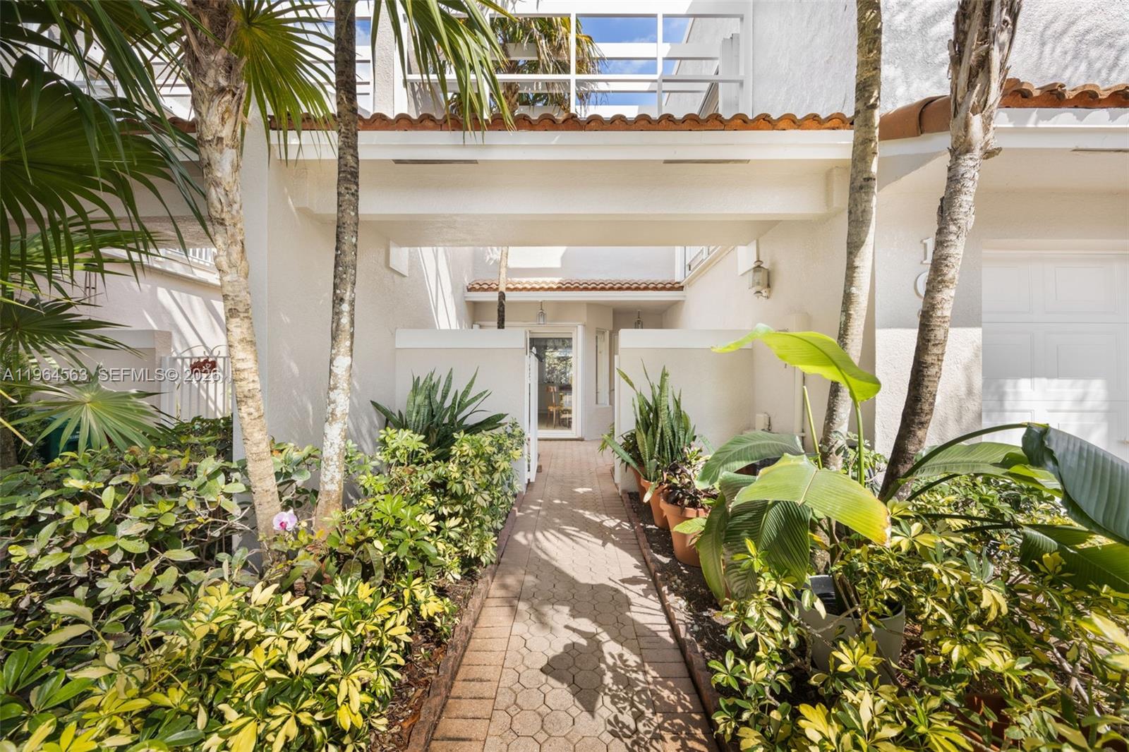 A paved walkway leads through a lush garden toward the entrance of a white building — 10233 NW 52nd Ln, Doral FL 33178, DORAL, FL