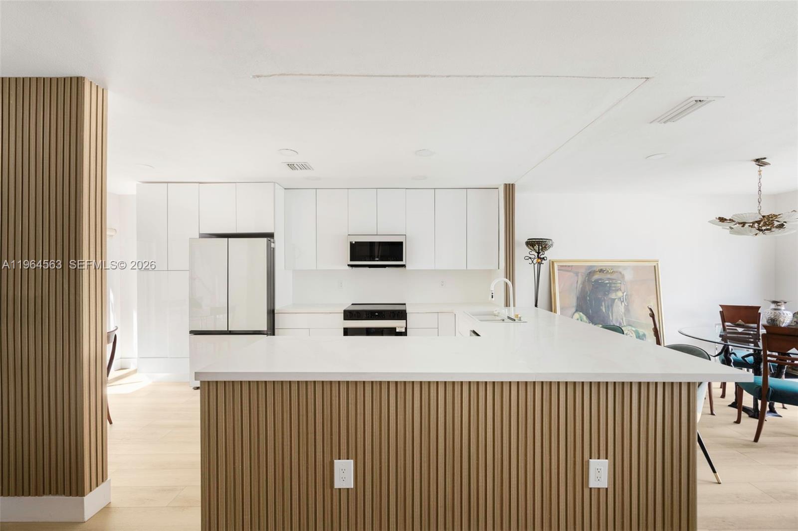 A modern kitchen features white cabinetry, a white countertop island, and wood-slatted paneling — 10233 NW 52nd Ln, Doral FL 33178, DORAL, FL