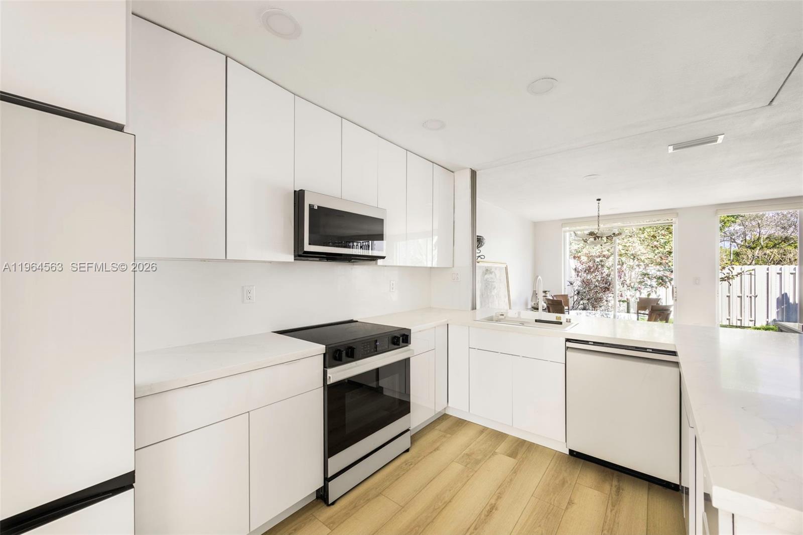 A modern kitchen features white flat-panel cabinetry, stainless steel appliances, and light wood-look flooring — 10233 NW 52nd Ln, Doral FL 33178, DORAL, FL