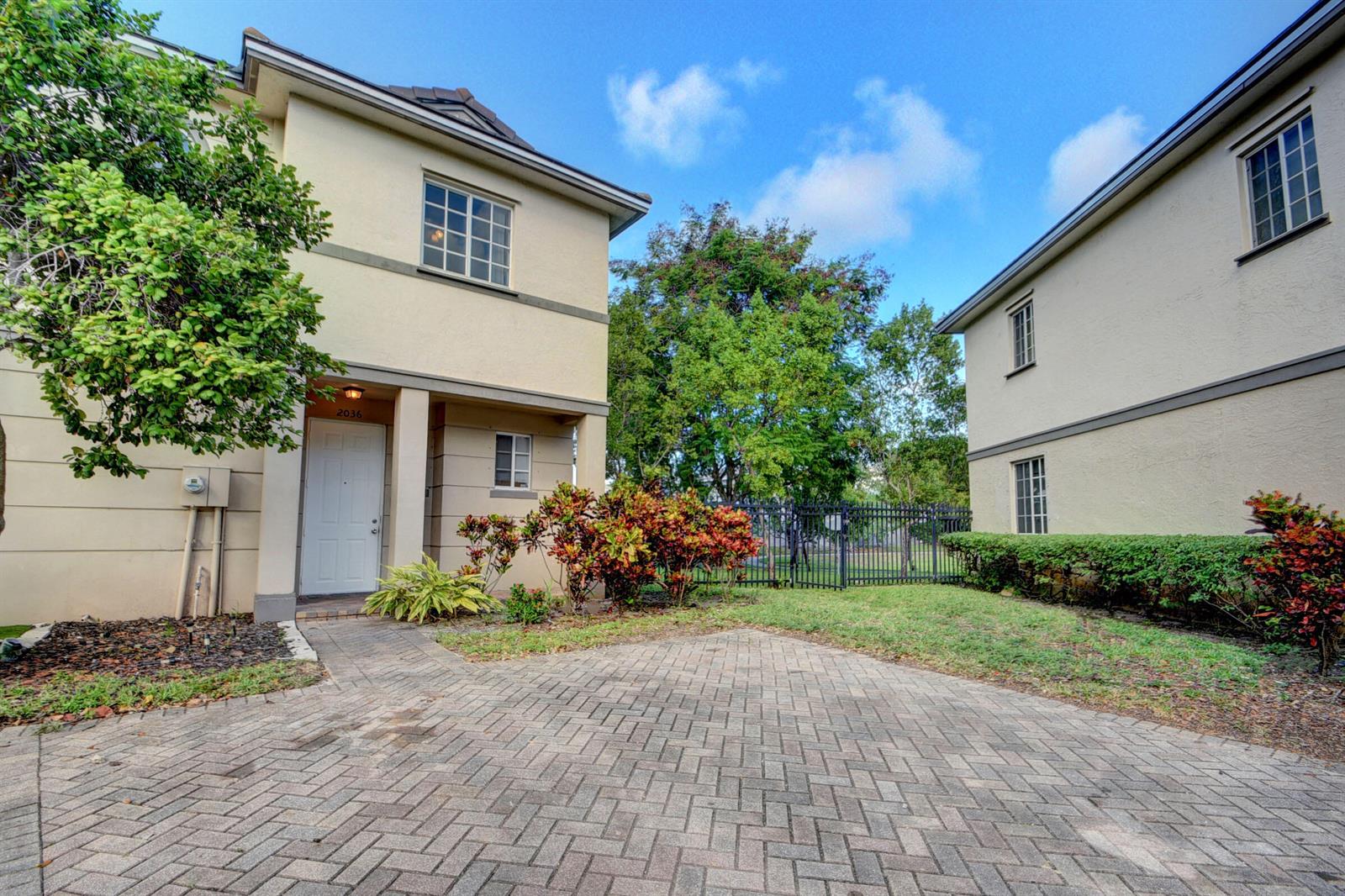 A paved courtyard sits between two two-story stucco buildings with a black metal fence behind — 2036 Marsh Harbor Drive, West Palm Beach FL 33404, WEST PALM BEACH, FL