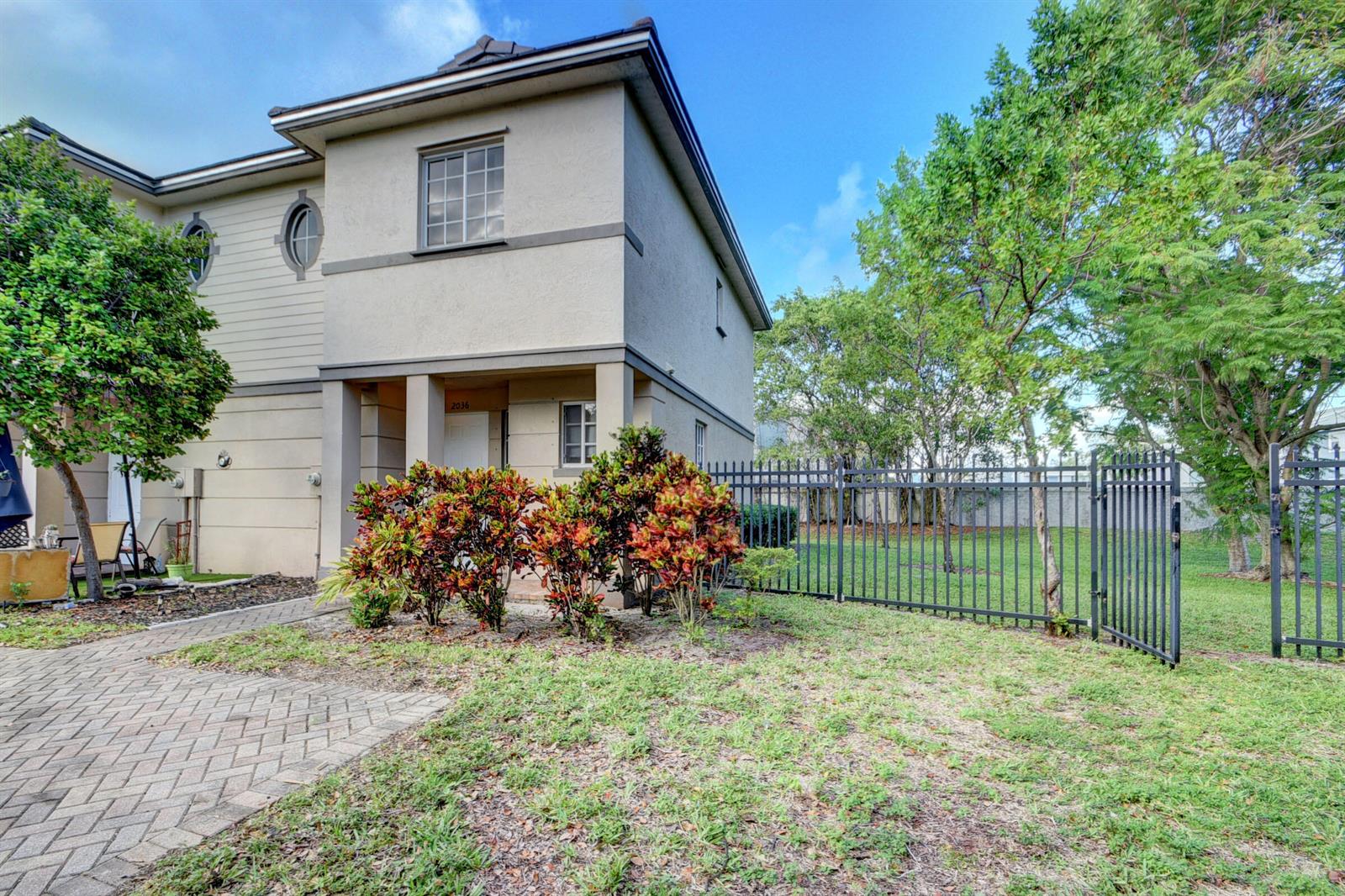 A two-story townhouse exterior with a paved walkway, landscaped bushes, and a black metal fence — 2036 Marsh Harbor Drive, West Palm Beach FL 33404, WEST PALM BEACH, FL