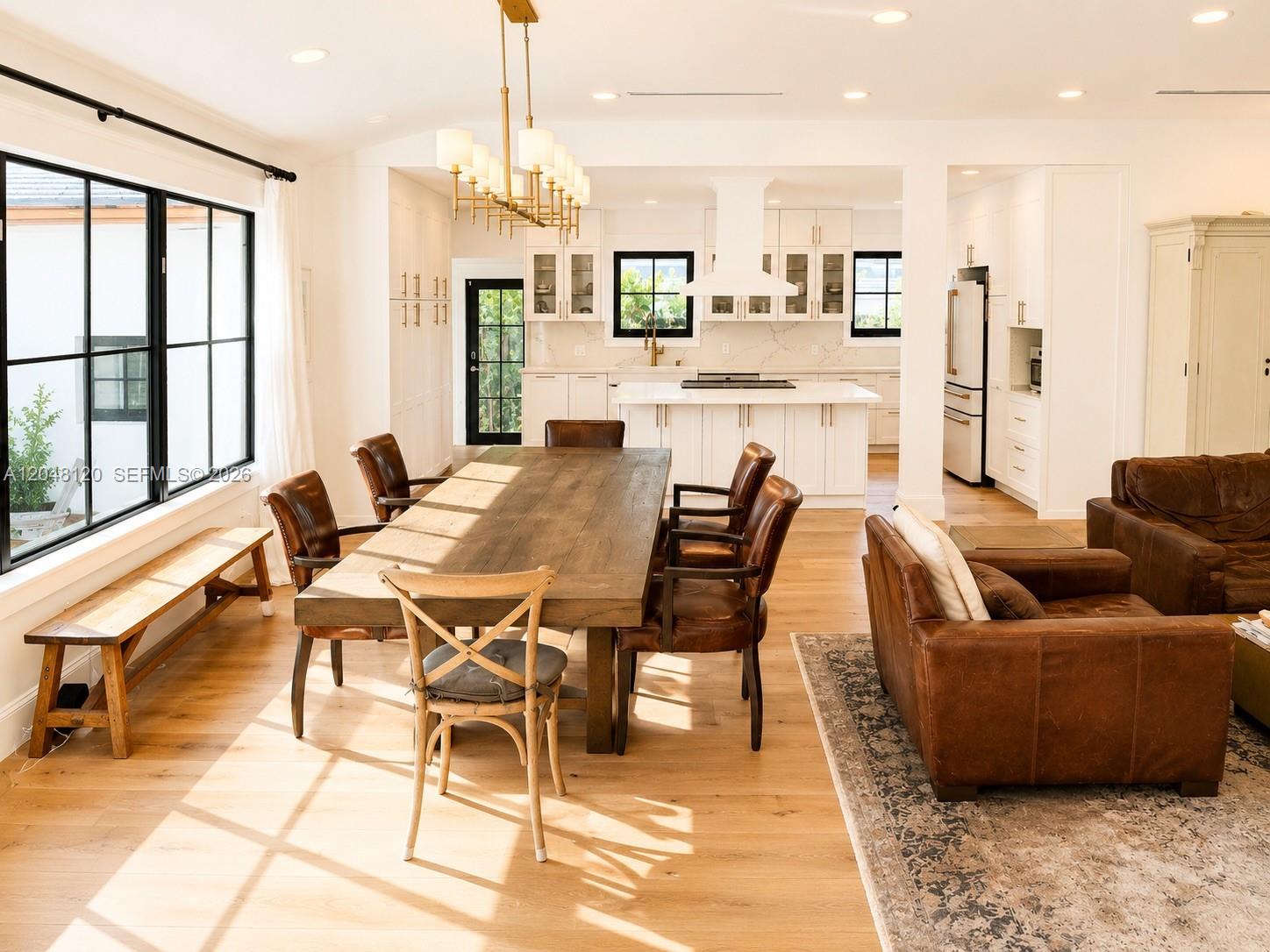 A bright open-concept dining and living area features a wooden table, leather chairs, and kitchen — 4455 N Bay Rd, Miami Beach FL 33140, MIAMI BEACH, FL