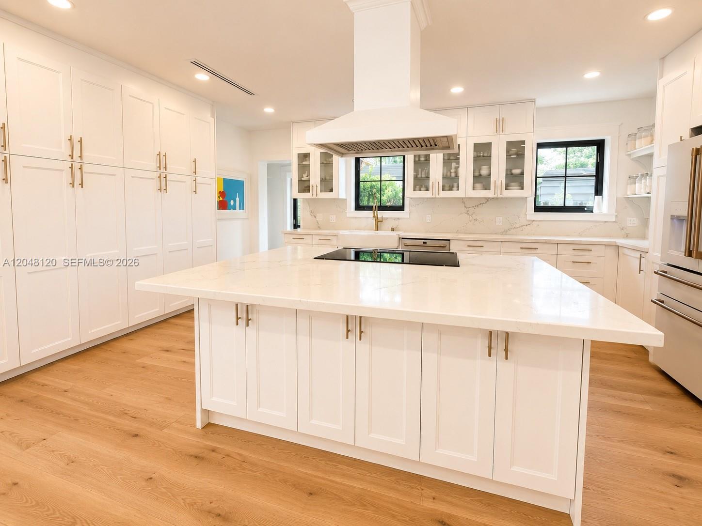 A modern white kitchen features a large center island, quartz countertops, and light wood flooring — 4455 N Bay Rd, Miami Beach FL 33140, MIAMI BEACH, FL