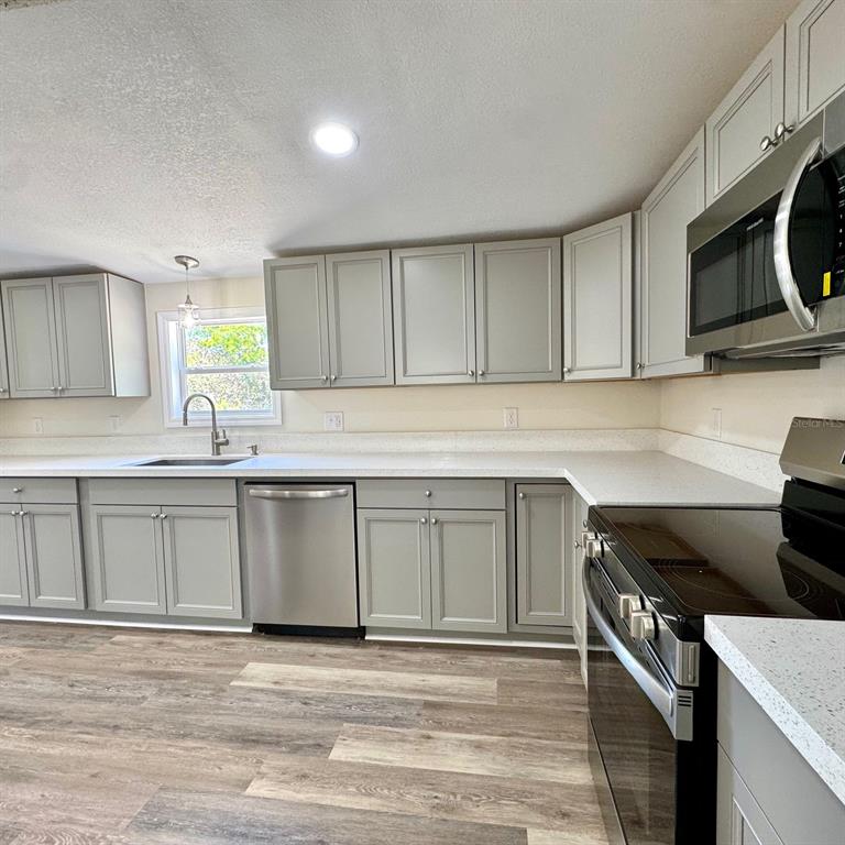 A kitchen features light gray cabinets, white countertops, stainless steel appliances, and wood-look flooring — 4220 OLD DIXIE HIGHWAY, AUBURNDALE, FL