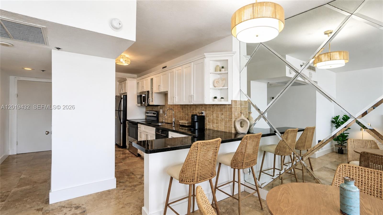 A kitchen features white cabinets, black countertops, a tiled backsplash, and a mirrored breakfast bar — 100 Lincoln Rd # 1206, Miami Beach FL 33139, MIAMI BEACH, FL