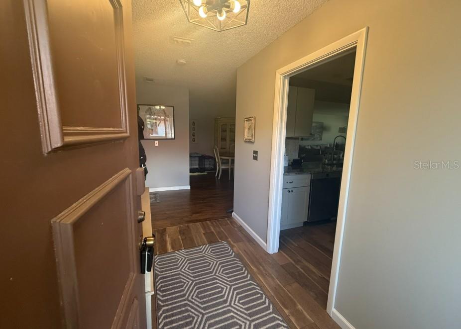 An entryway with wood-look flooring leads to a kitchen on the right and dining area — 3500 EL CONQUISTADOR PARKWAY UNIT 124, BRADENTON, FL