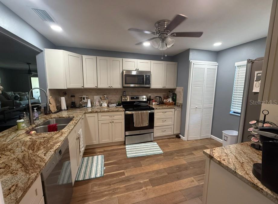 A kitchen features cream cabinets, granite countertops, stainless steel appliances, and wood-look tile flooring — 3500 EL CONQUISTADOR PARKWAY UNIT 124, BRADENTON, FL