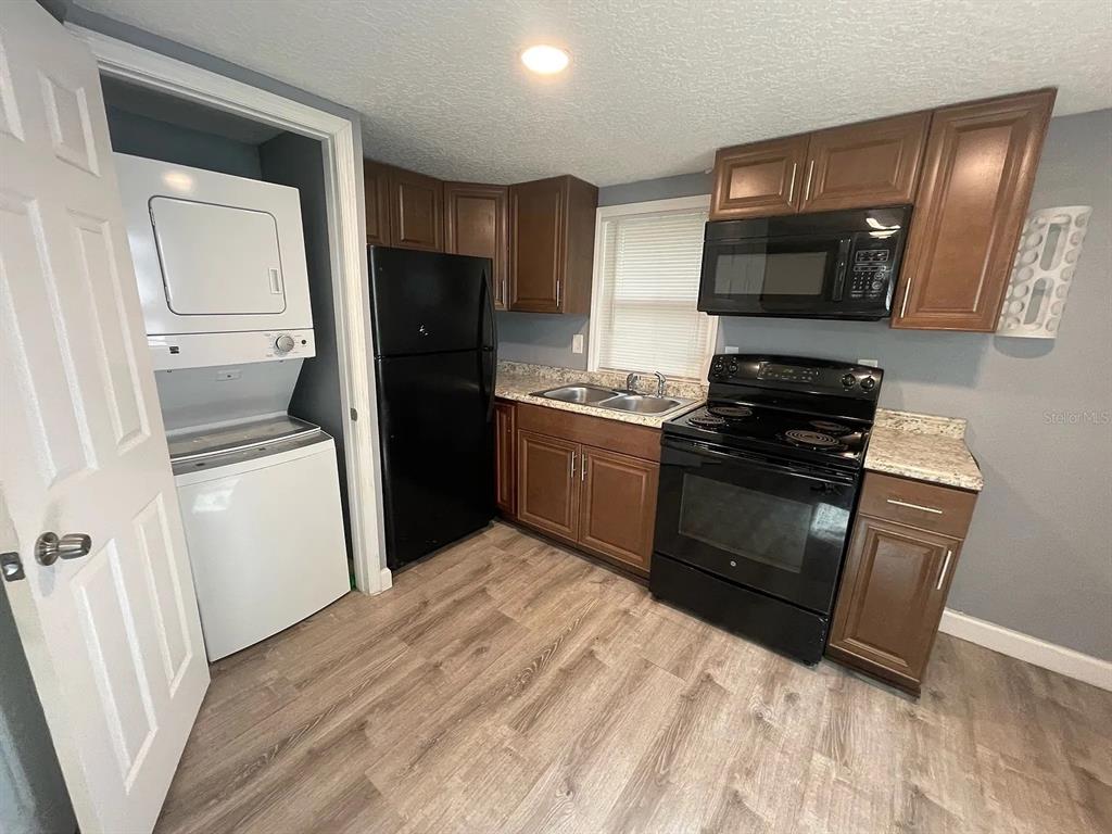 A kitchen with wood cabinets, black appliances, a stacked washer-dryer, and wood-look flooring — 1020 W PORTAGE STREET UNIT C, KISSIMMEE, FL