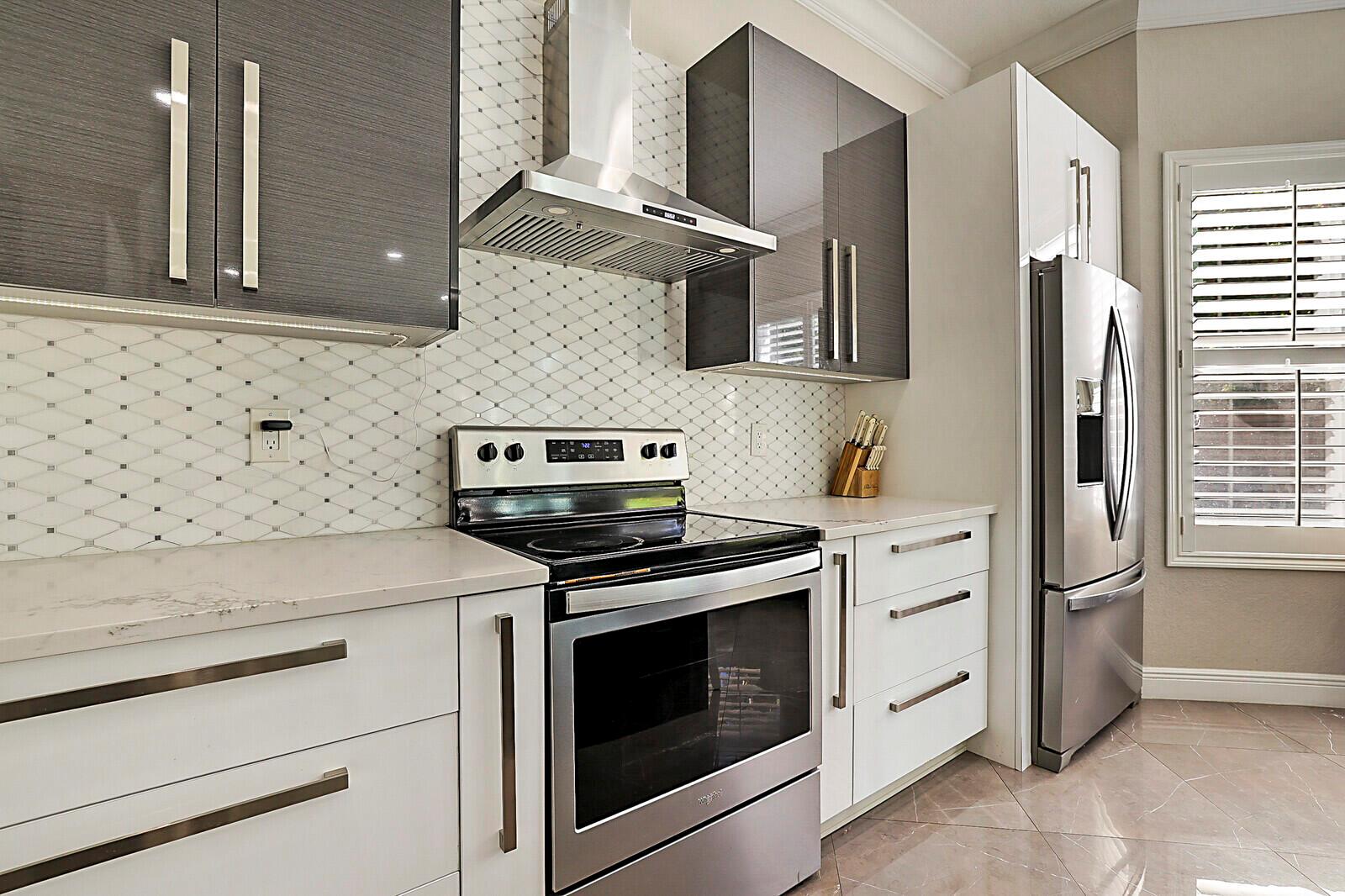 A modern kitchen features two-tone cabinetry, a large island, and a view of a pool — 7167 Ivy Crossing Lane, Boynton Beach FL 33436, BOYNTON BEACH, FL