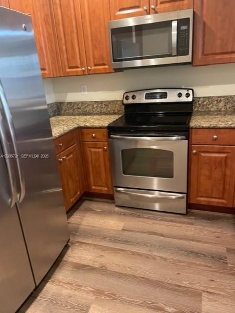 A kitchen features wood cabinets, stainless steel appliances, and wood-look flooring — SUNRISE, FL