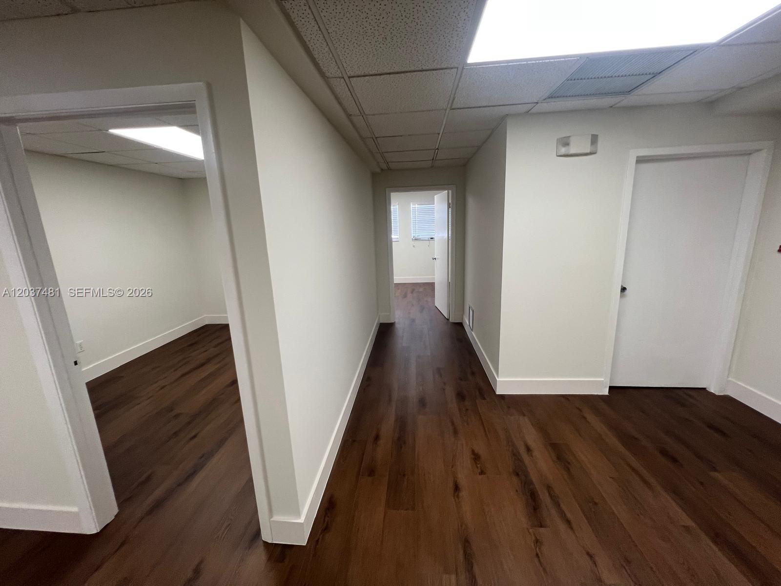 A hallway with dark wood-look flooring leads to a room with white walls and doors — 145 Madeira Ave # 202, Coral Gables FL 33134, CORAL GABLES, FL