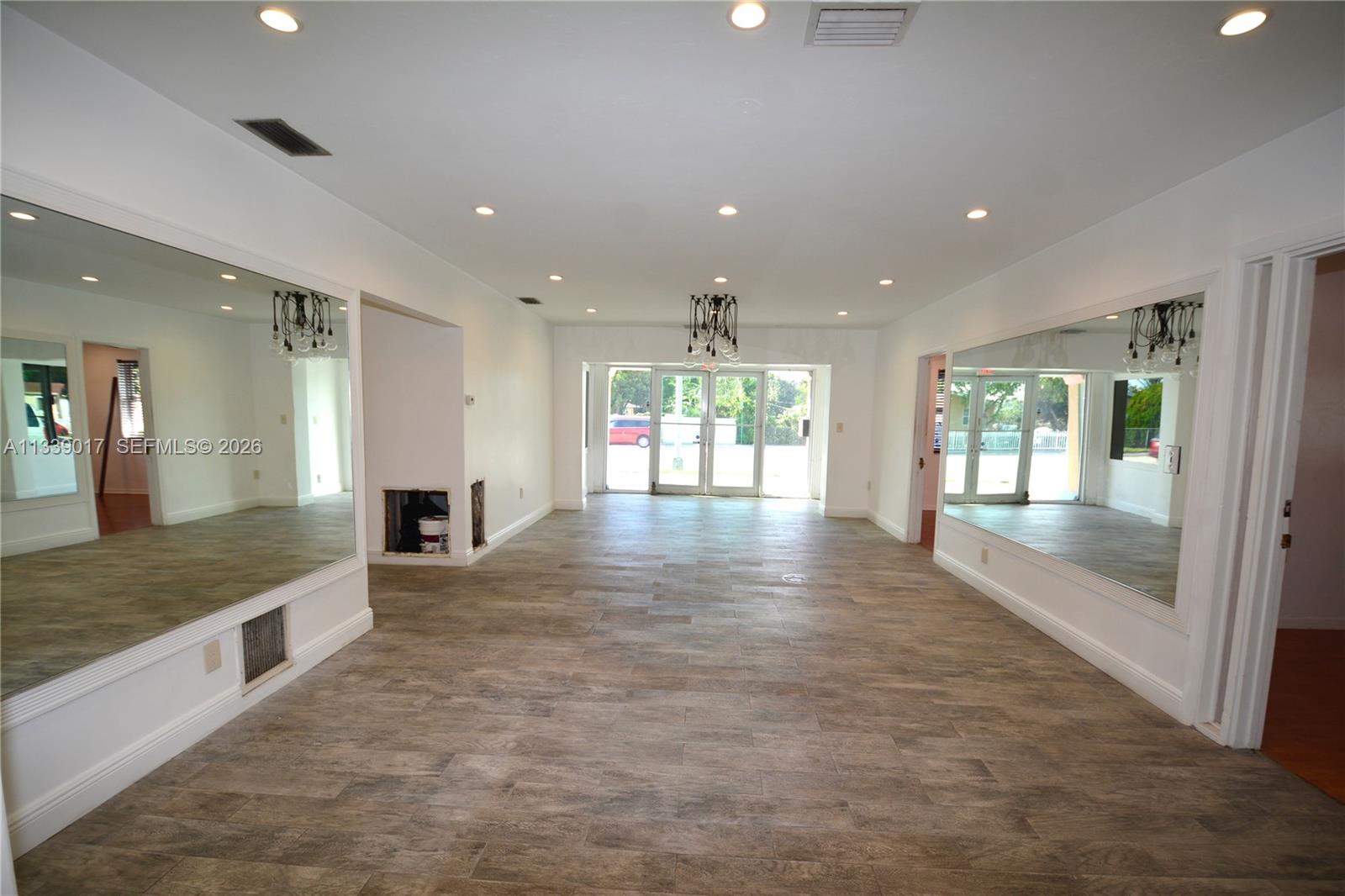 A spacious room features wood-look tile flooring, recessed lighting, and large wall-mounted mirrors — 16921 NE 6th Ave, North Miami Beach FL 33162, NORTH MIAMI BEACH, FL