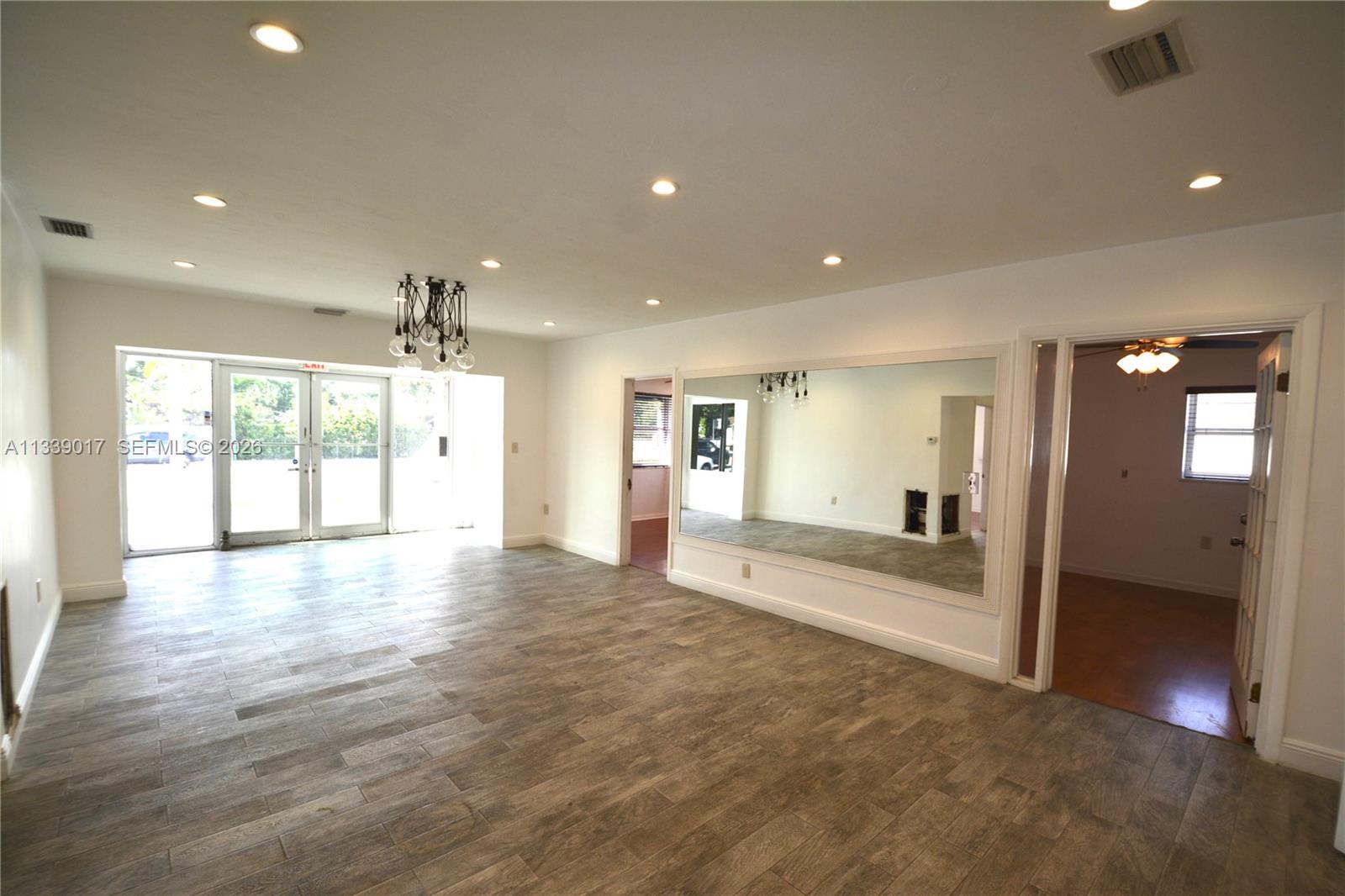 A living room features wood-look tile flooring, recessed lighting, a large wall mirror, and glass doors — 16921 NE 6th Ave, North Miami Beach FL 33162, NORTH MIAMI BEACH, FL
