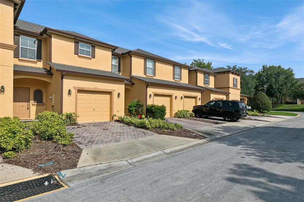 A row of tan townhouses with attached garages and paved driveways under a blue sky — 1250 TWIN TREES LANE, SANFORD, FL