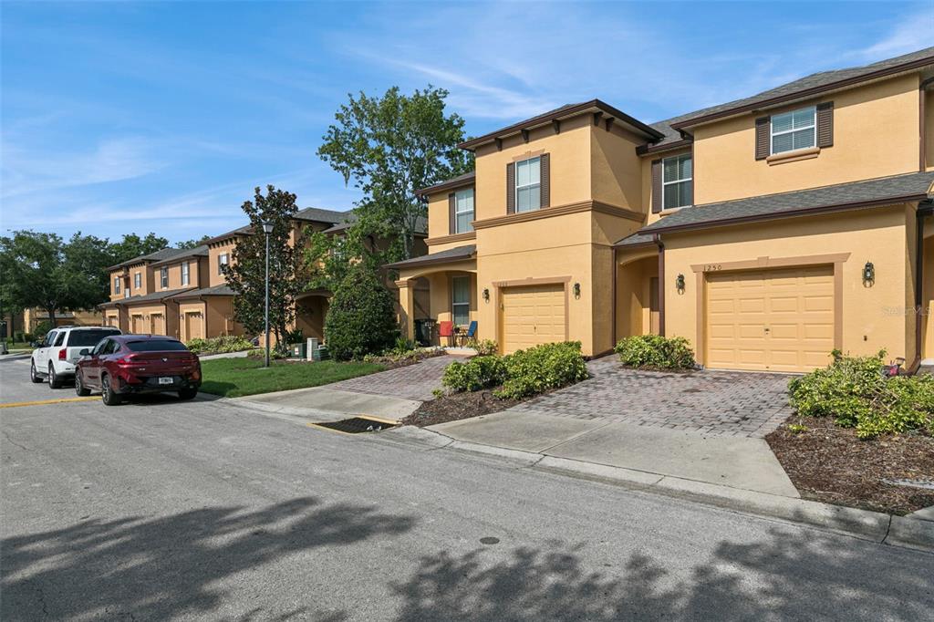 A row of two-story tan townhomes with attached garages and paved driveways under a blue sky — 1250 TWIN TREES LANE, SANFORD, FL