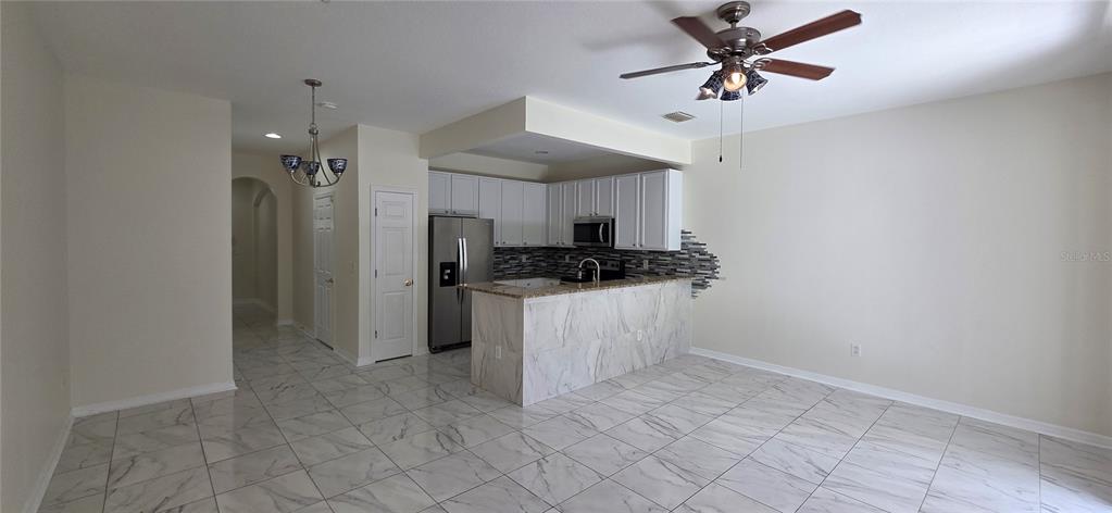 A kitchen with white cabinets and a marble-patterned island overlooks a tiled living area — 2027 STRATHMILL DRIVE, CLEARWATER, FL