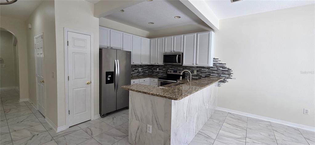 A kitchen features white cabinets, stainless steel appliances, granite countertops, and a marble-patterned island — 2027 STRATHMILL DRIVE, CLEARWATER, FL