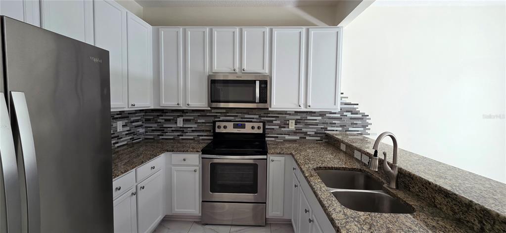 A kitchen features white cabinets, stainless steel appliances, granite countertops, and a mosaic tile backsplash — 2027 STRATHMILL DRIVE, CLEARWATER, FL