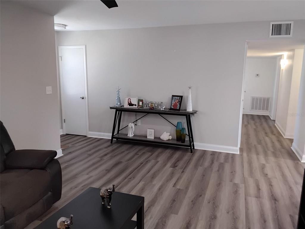 A living room features gray wood-look flooring, a console table, and a doorway leading down a hallway — 702 CYPRESS PLACE, SUN CITY CENTER, FL