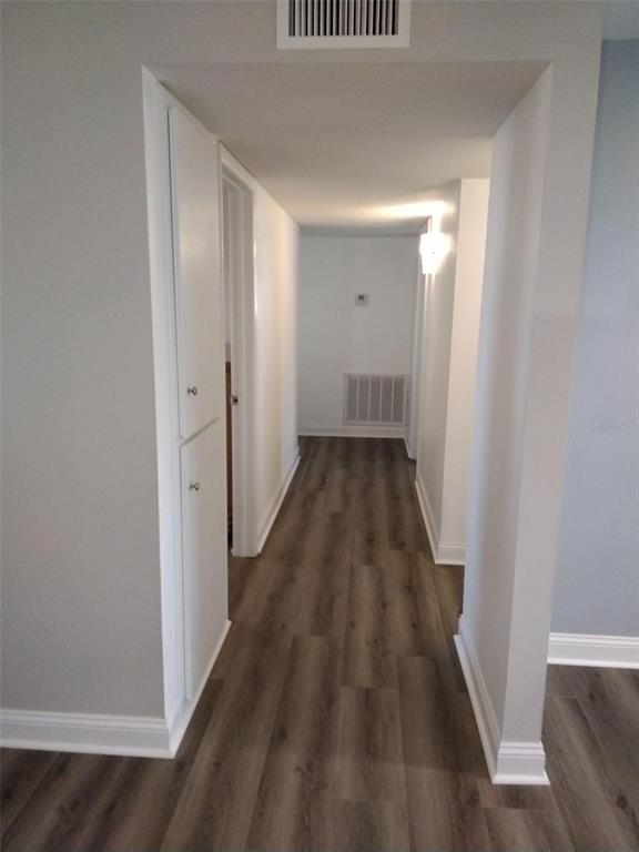 A hallway with wood-look flooring, white walls, a built-in cabinet, and a ceiling vent — 702 CYPRESS PLACE, SUN CITY CENTER, FL